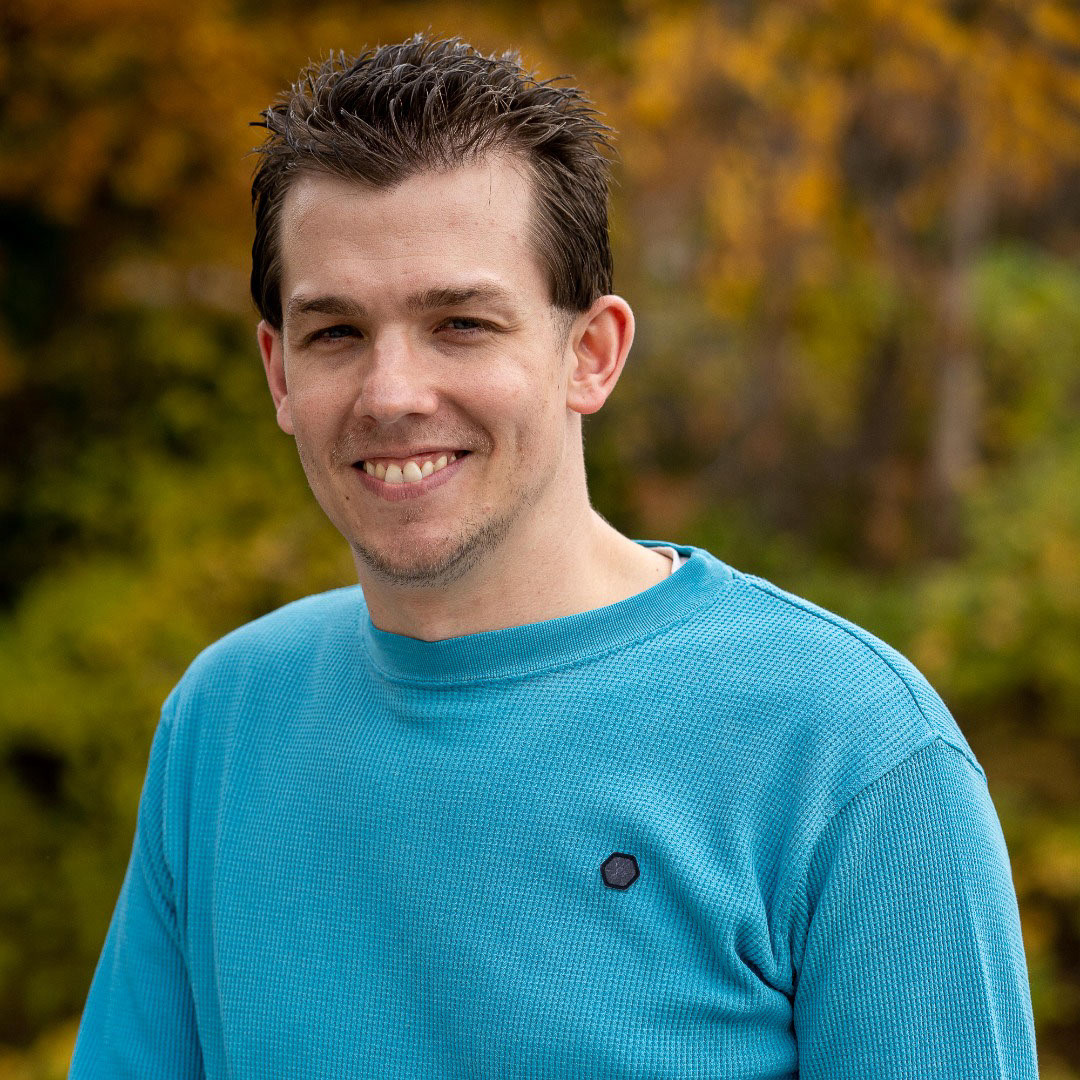 man in blue shirt with fall foilage in background 