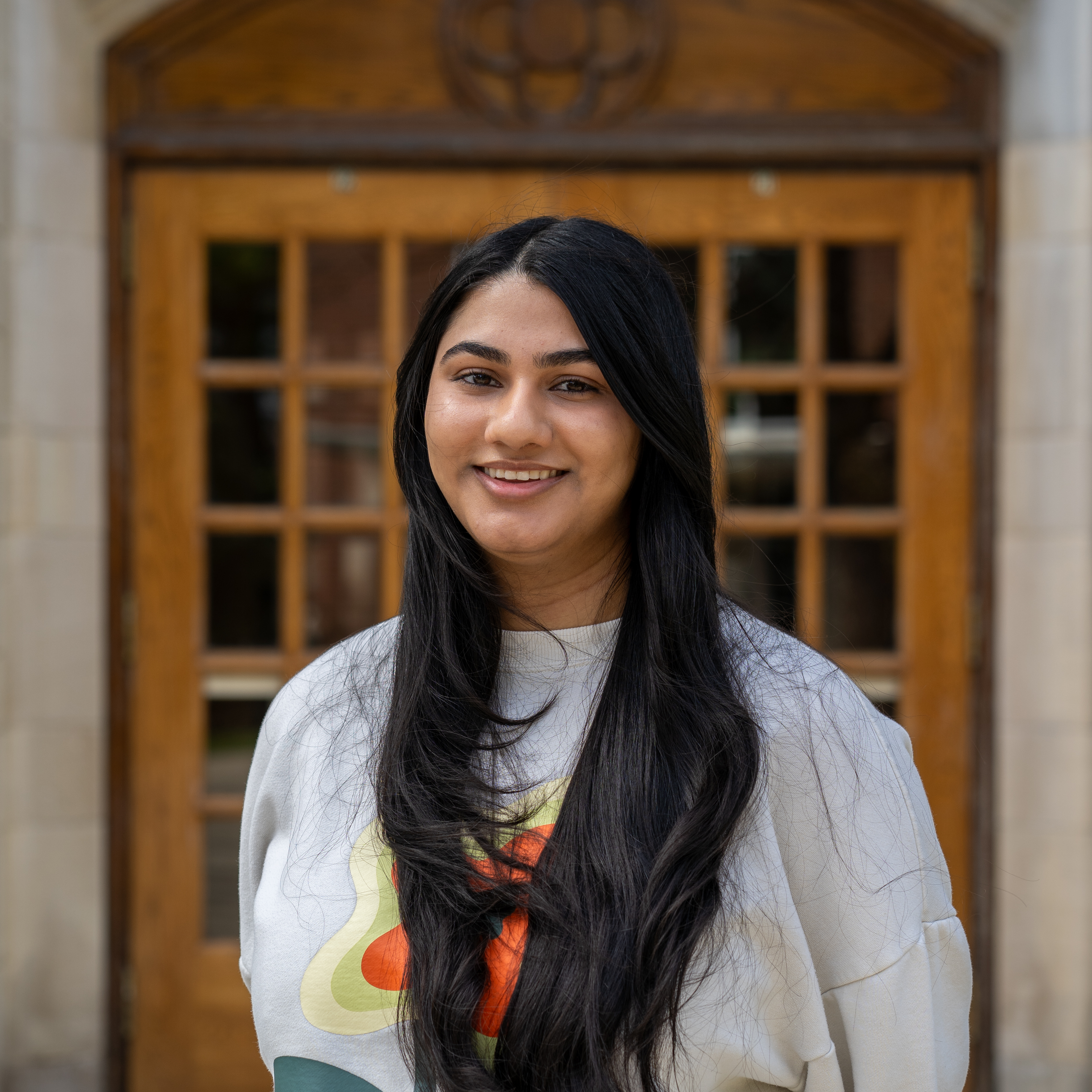 Female student smiling outside in front of a wooden door.